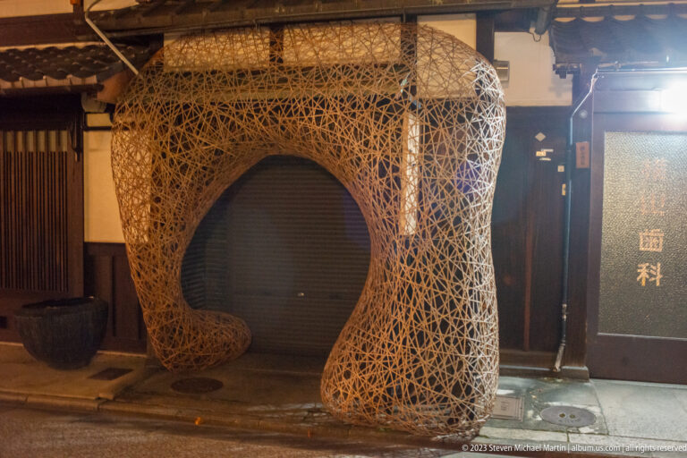 Woven sculptural installation shown at night with the principal architectural, landscape, or street details visible in the composition.