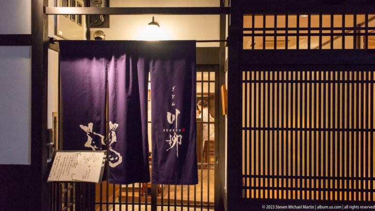 Traditional entrance with purple noren shown at night with the principal architectural, landscape, or street details visible in the composition.