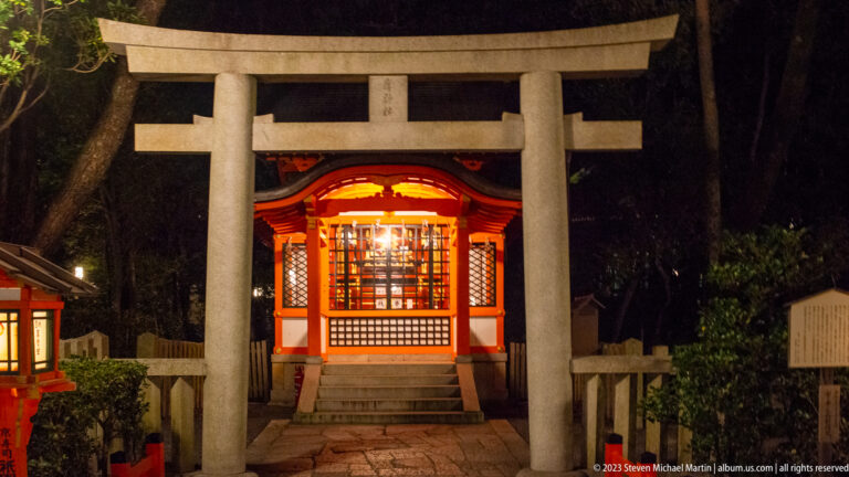 Small Yasaka Shrine beyond stone torii shown at night with the principal architectural, landscape, or street details visible in the composition.