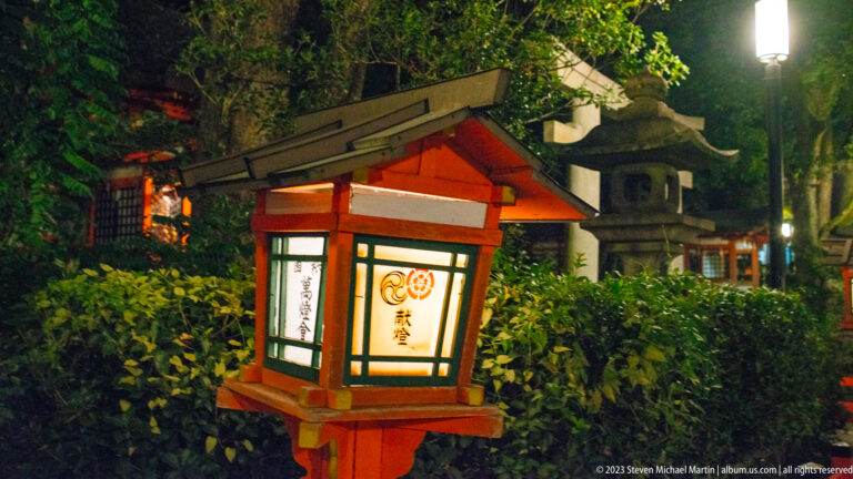 Traditional Yasaka Shrine lantern beside stone lantern shown at night with the principal architectural, landscape, or street details visible in the composition.
