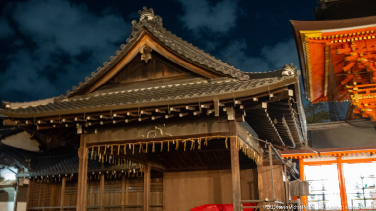 Traditional wooden auxiliary Yasaka Shrine hall shown at night with the principal architectural, landscape, or street details visible in the composition.