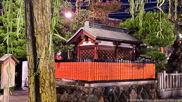 Small Yasaka Shrine enclosed by vermilion fence shown at night with the principal architectural, landscape, or street details visible in the composition.