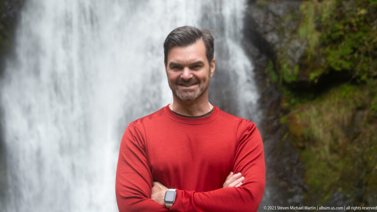 Man in a red shirt and wristwatch posing with folded arms before Choshi Falls.