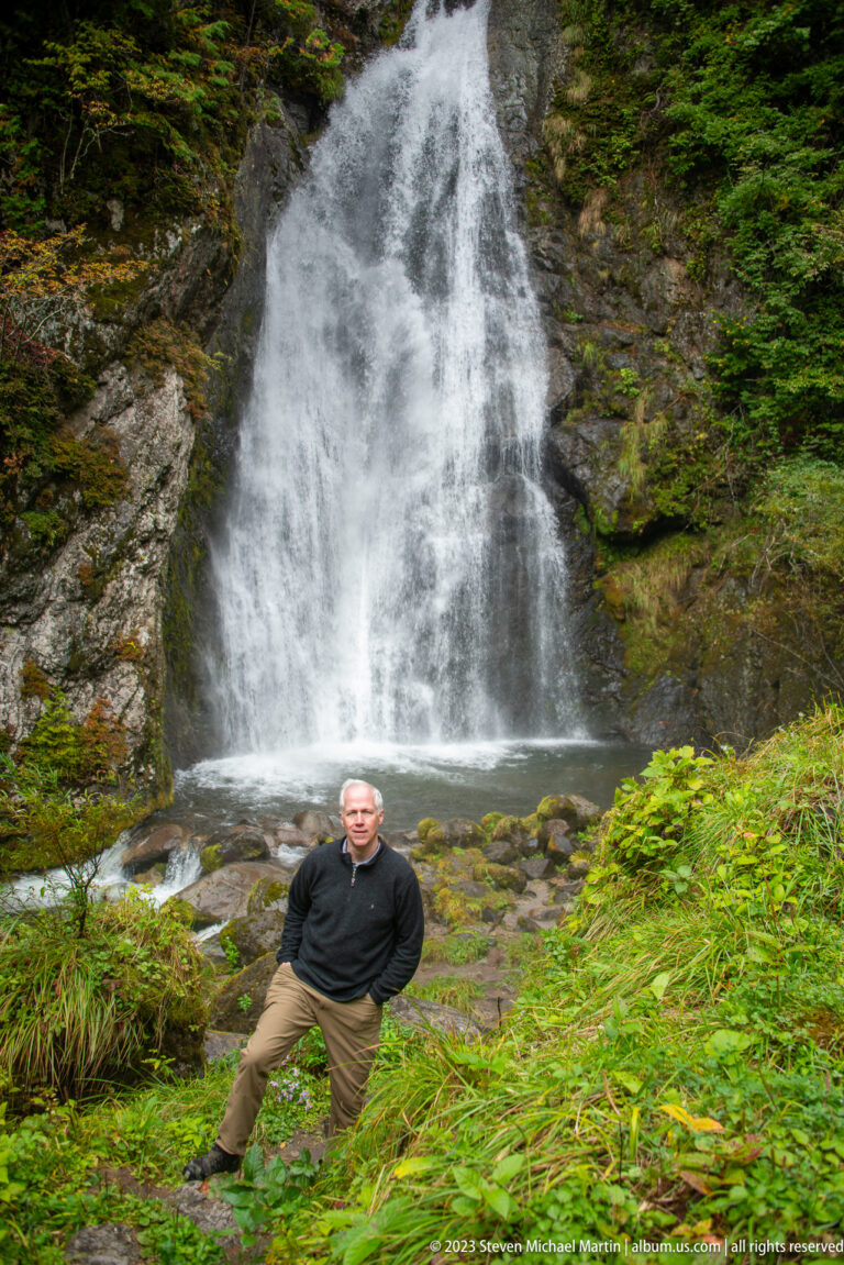Man standing on a grassy bank below the broad cascade of Choshi Falls.