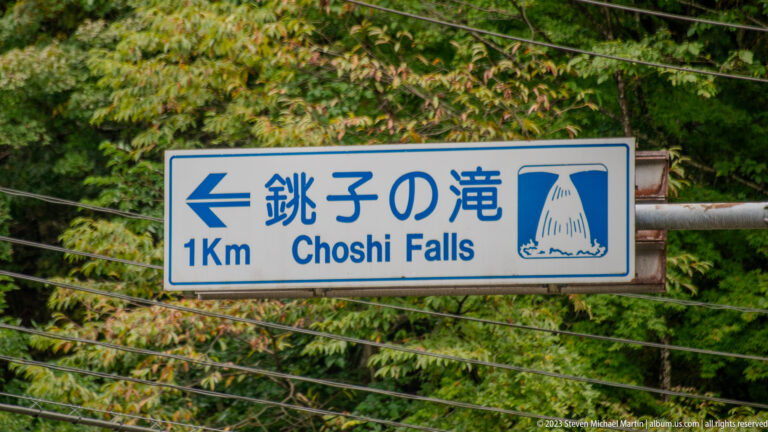 Blue-and-white bilingual sign pointing left to Choshi Falls, one kilometer away.