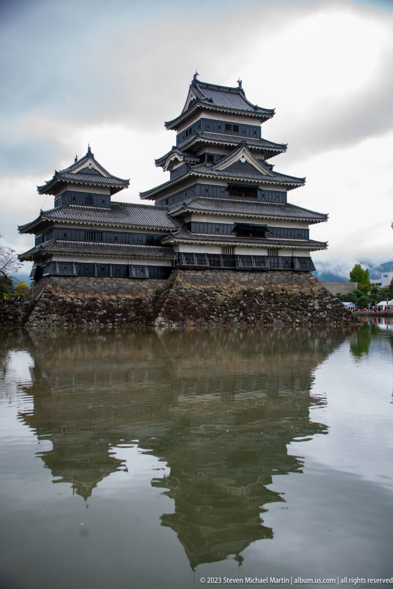 Broadside view of Matsumoto Castle and its layered roofs reflected in calm moat water.