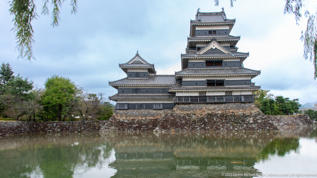 Centered view of Matsumoto Castle across the moat with willow branches above.