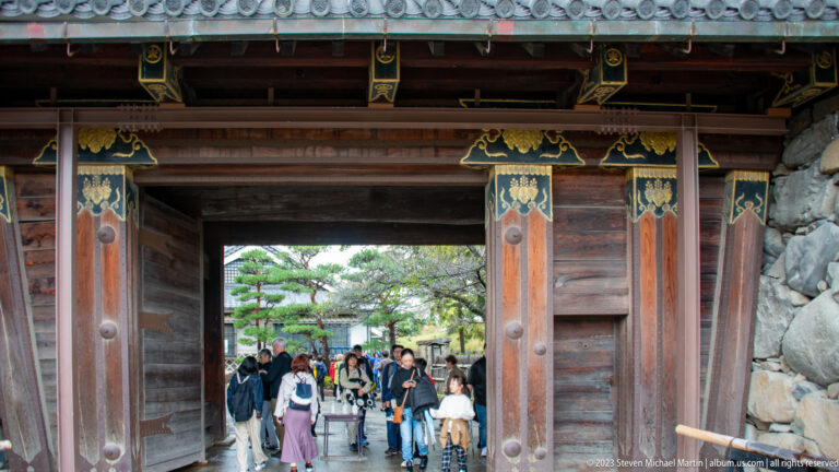Visitors walking through a decorated wooden gateway into Matsumoto Castle grounds.
