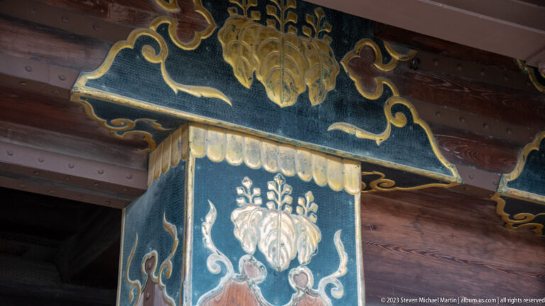 Close detail of blue-green and gold painted ornament on a timber gate post.