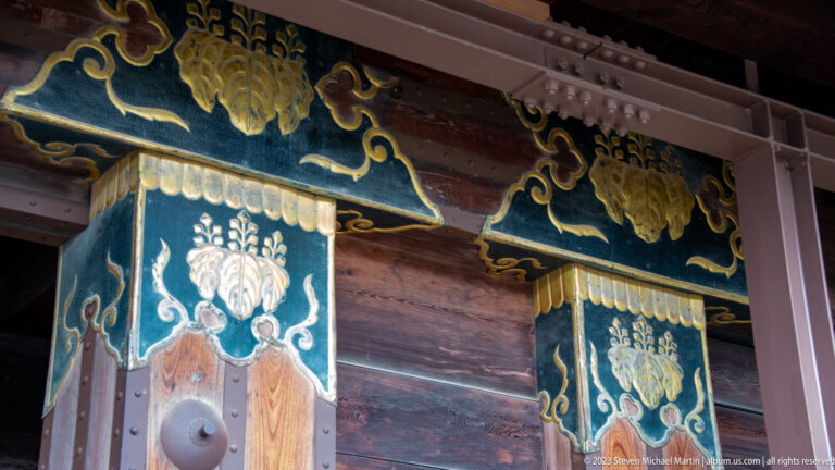 Two decorated timber gate posts with blue-green panels, gold motifs, and visible beams.