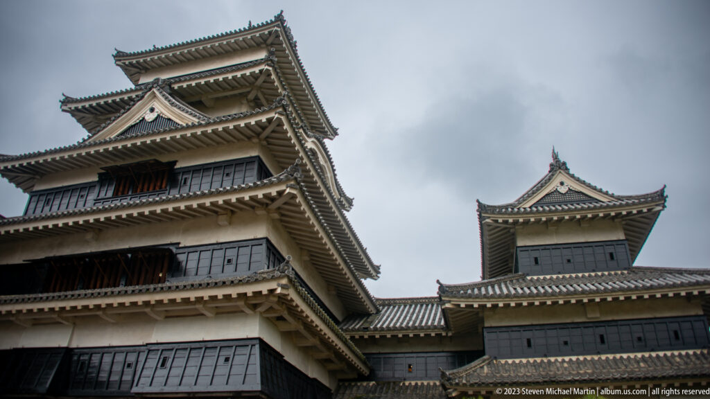 Low-angle view of two connected Matsumoto Castle towers with overlapping tiled roofs and black-and-white walls.
