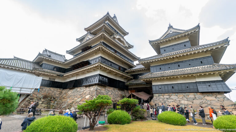 Visitors queue below Matsumoto Castle’s stone base and connected black-and-white towers.