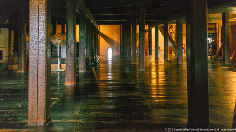 Long dim gallery inside Matsumoto Castle with rows of timber posts, beams, and a reflective wooden floor.
