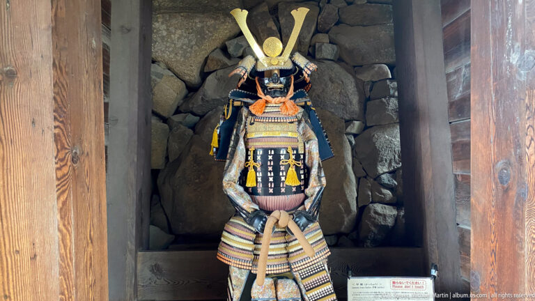 Complete samurai armor with a crescent-crested helmet displayed in a timber-framed stone alcove inside Matsumoto Castle.