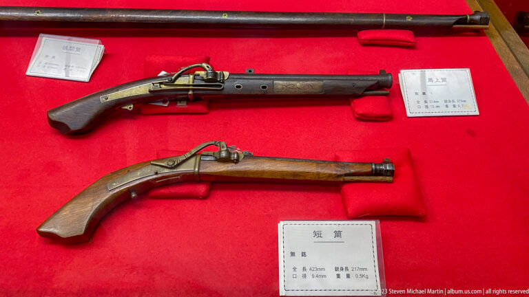 Long and short Japanese matchlock firearms with wooden stocks and metal mechanisms displayed on red fabric.