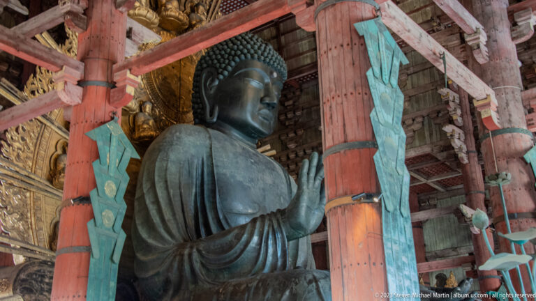 Todai-ji’s seated bronze Daibutsu framed by red columns, turquoise hangings, and a gilded halo.