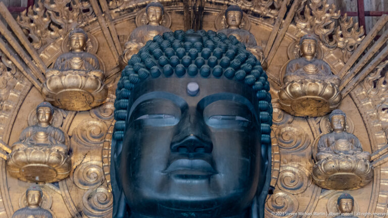 Close view of Todai-ji’s bronze Buddha face surrounded by small gilded seated figures.