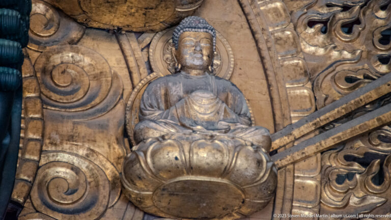 Seated gilded Buddha on a lotus pedestal amid radiating halo ribs and flame motifs.