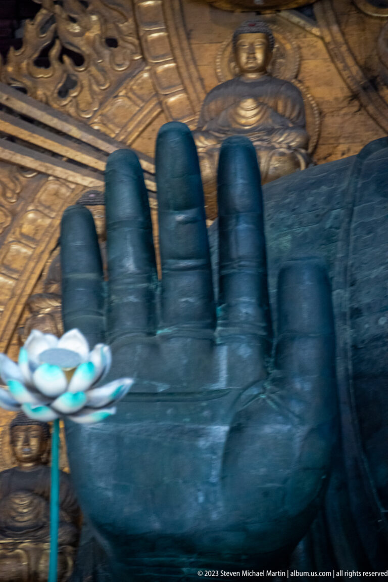 Enormous raised bronze hand of Todai-ji’s Daibutsu with gilded halo figures behind.