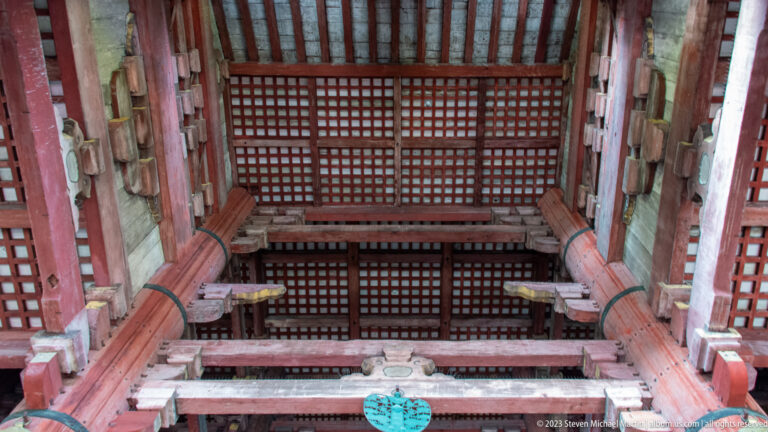 Upward view of red timber columns, beams, rafters, and lattice ceiling inside the Great Buddha Hall.