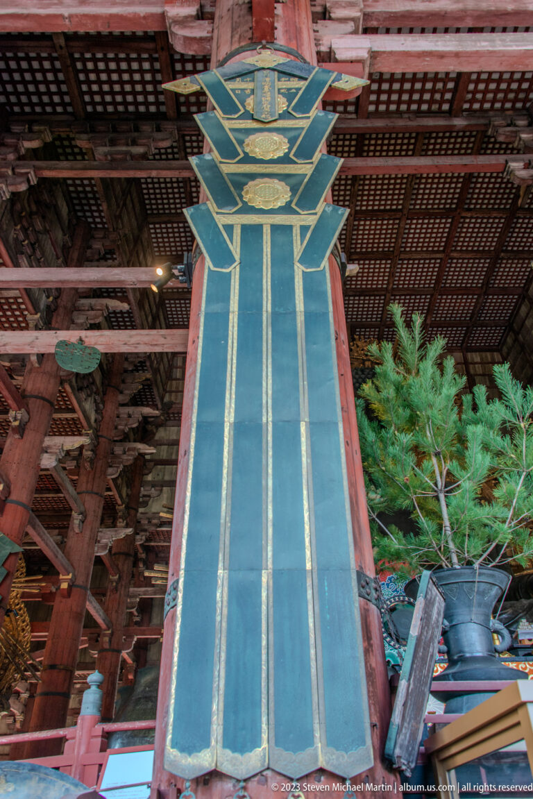 Long blue and gold ceremonial temple banner hanging between red columns beneath a lattice ceiling.