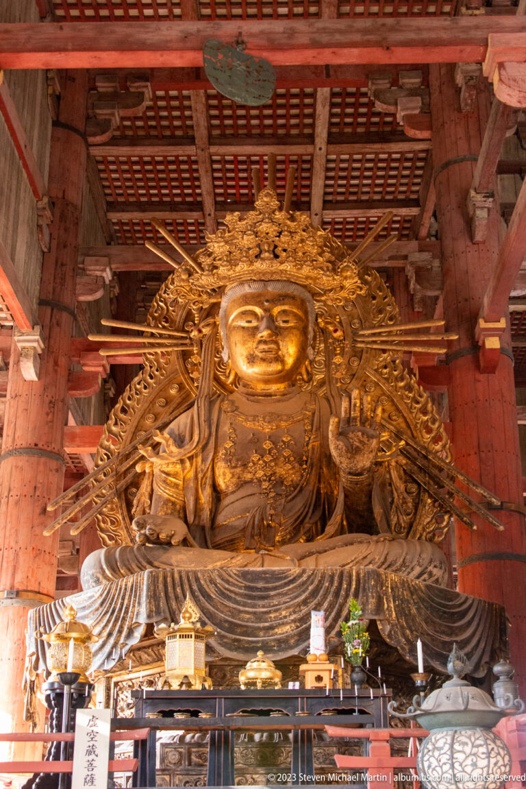 Monumental gilded crowned bodhisattva seated on a lotus pedestal behind altar furnishings.