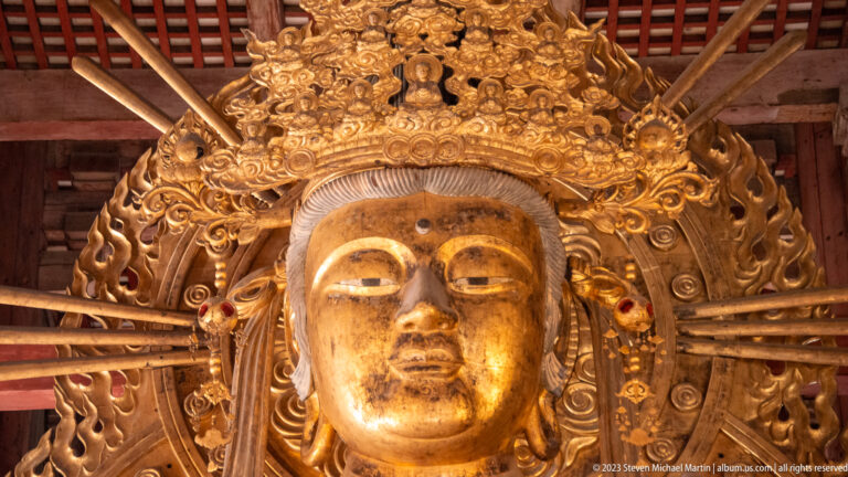 Close view of a gilded bodhisattva face framed by an elaborate crown and flame-like aureole.