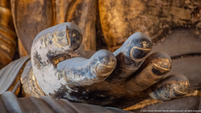 Close view of a monumental gilded sculpted hand with worn surface and darkened finger recesses.