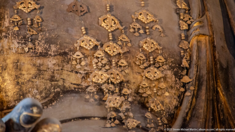 Clusters of small gilded floral pendants hanging against the dark surface of a Buddhist sculpture.