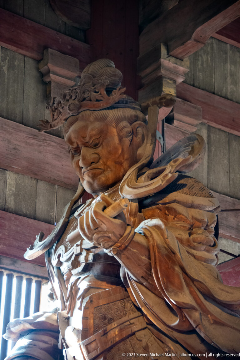 Side view of a monumental armored wooden guardian beneath the timber roof of Todai-ji.