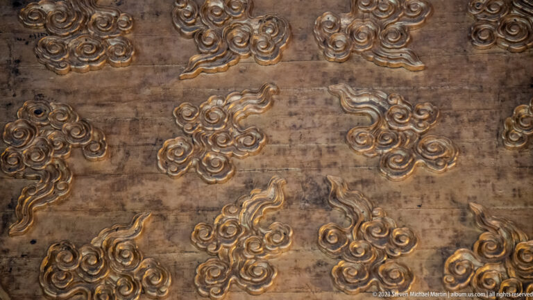 Raised gilded cloud motifs scattered across a dark weathered architectural surface.