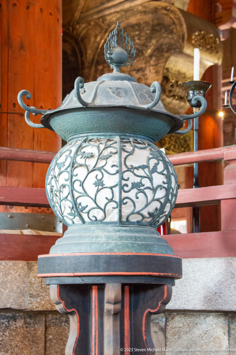 Decorative bronze temple lantern with openwork globe, lotus finial, and curved side arms.