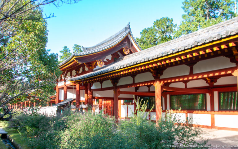 Vermilion-and-white covered temple corridor with gray tiled roofs and trees.