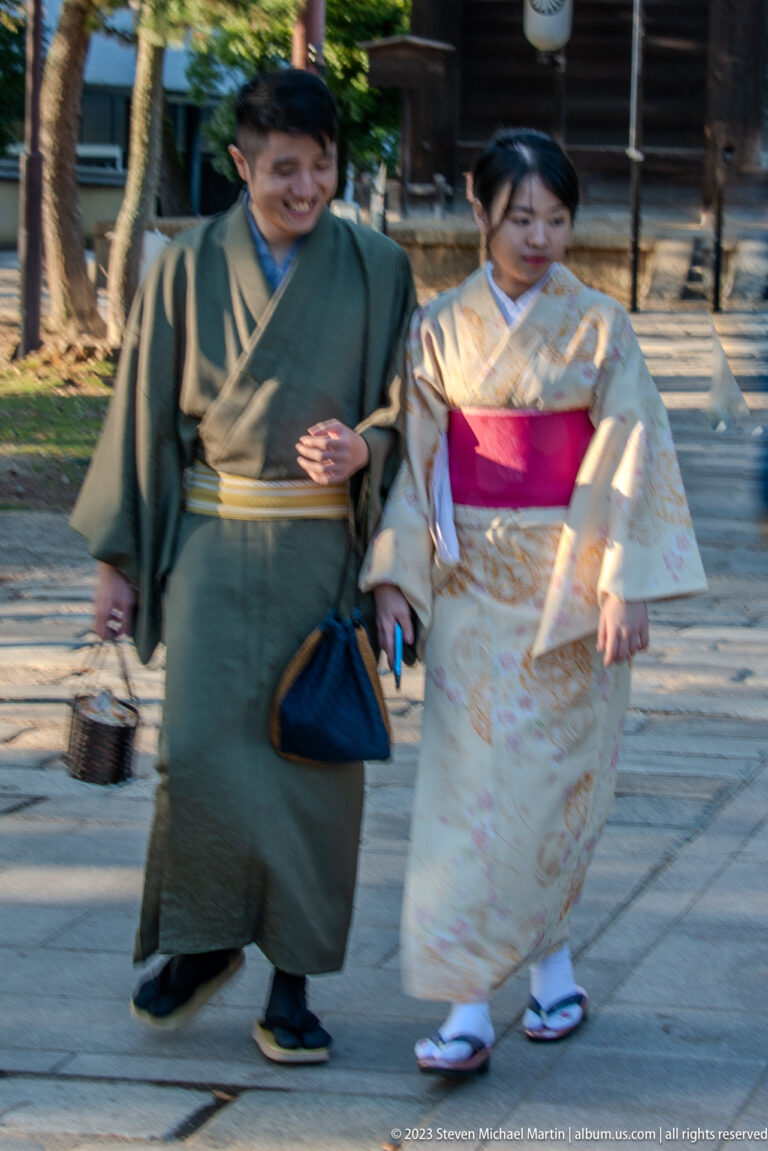 Two visitors in green and pale floral kimono walking together on a temple path.