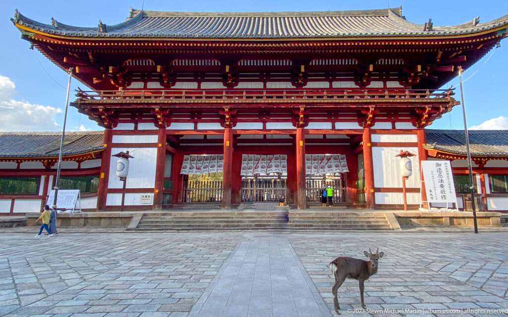 Sika deer crossing a stone forecourt before a monumental vermilion gate at Todai-ji.
