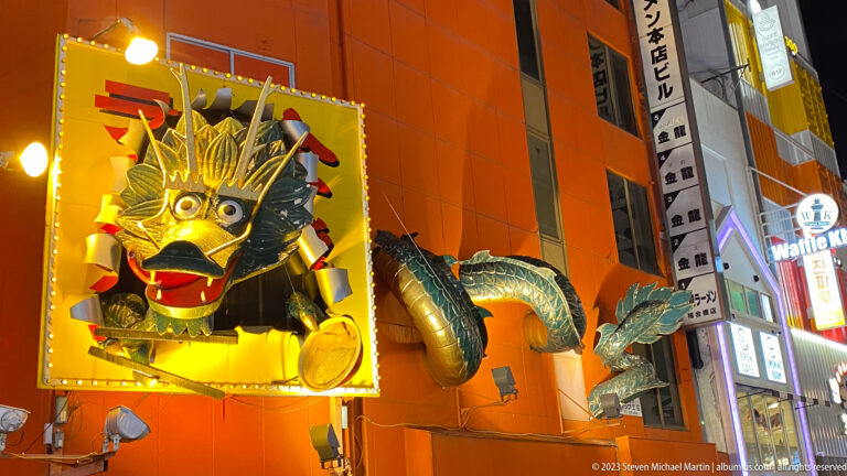 Illuminated dragon sculpture projecting from an orange Dotonbori building at night.