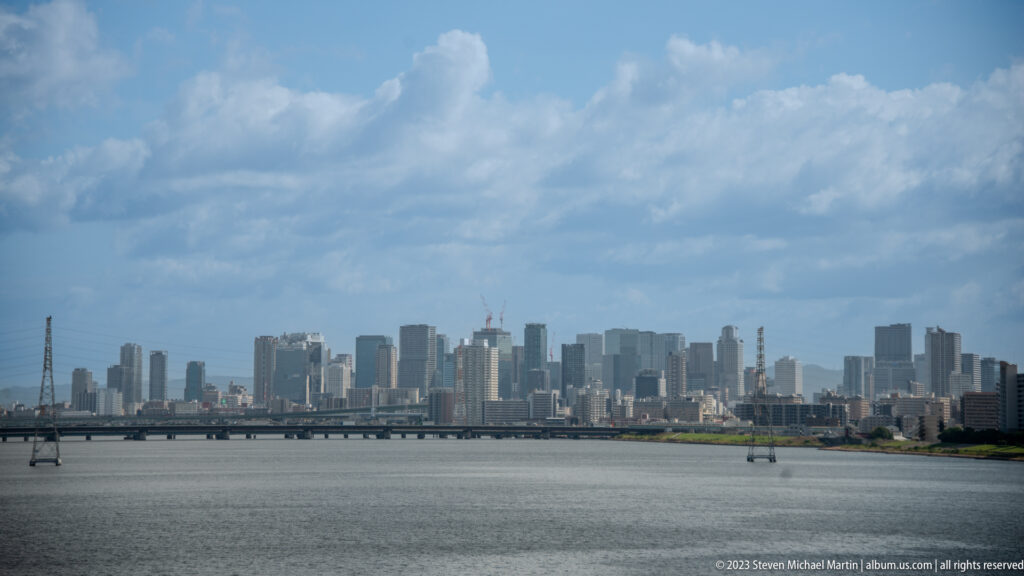 Closer view of Osaka high-rises across water beneath large cumulus clouds.