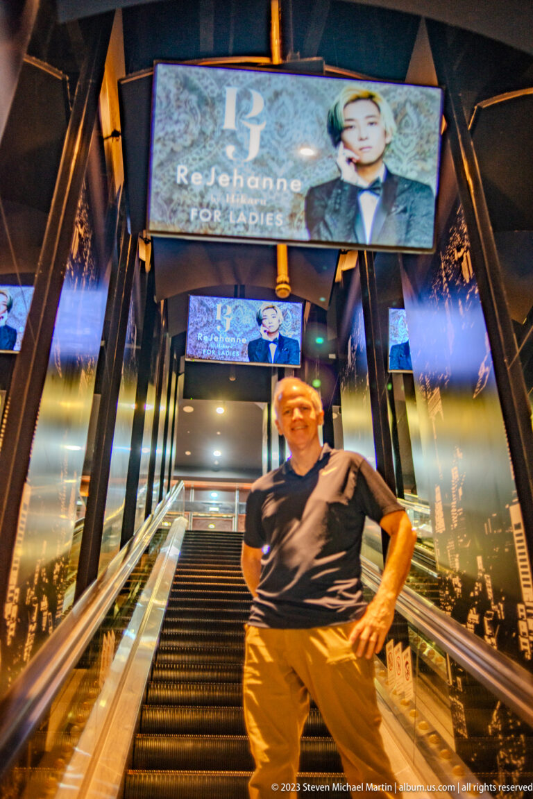 Visitor standing before a mirrored escalator beneath repeating fashion advertising screens.