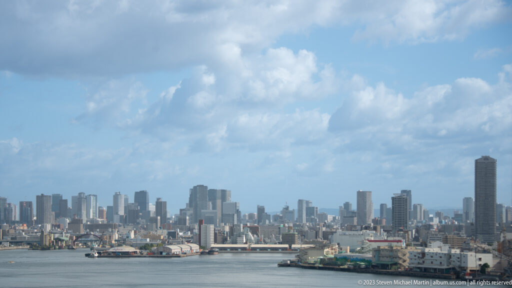 Osaka harbor and skyline with docks, high-rises, and large clouds.