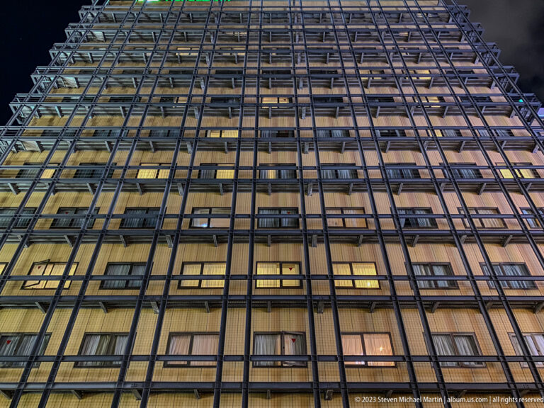 Upward view of a modern gridded high-rise façade with illuminated windows.
