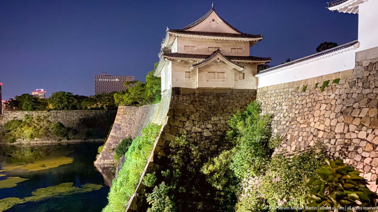 White Osaka Castle turret above stone ramparts and moat at night.