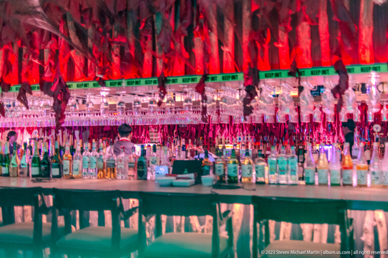 Liquor bottles and glassware beneath dense red decorations in an Osaka bar.