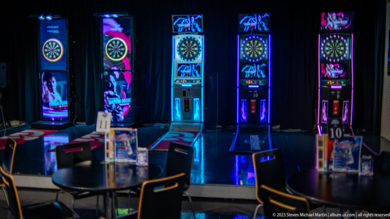 Four brightly illuminated electronic dart machines in a dark Osaka gaming venue.