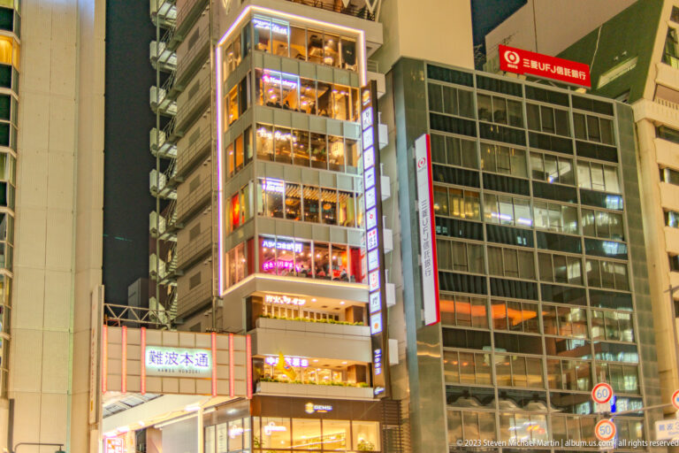 Narrow multi-storey restaurant building beside a Mitsubishi UFJ Bank sign in Osaka.