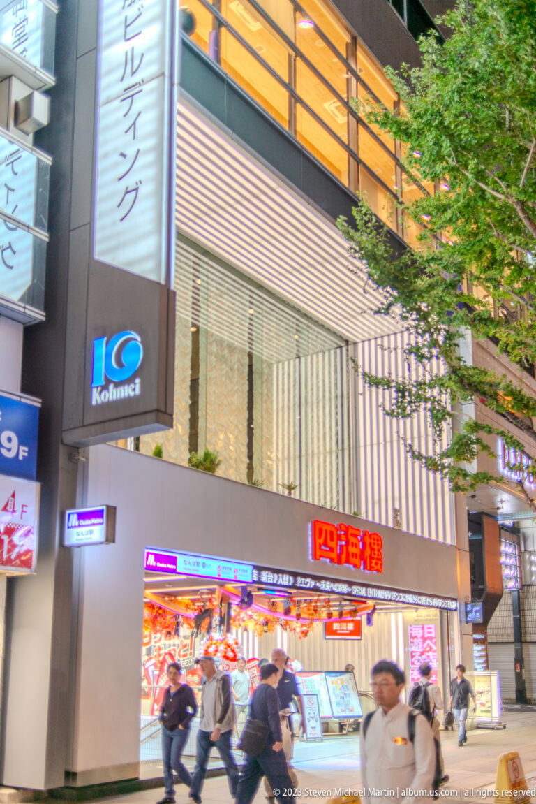 Kohnan-branded building above a bright restaurant entrance with pedestrians in Osaka.