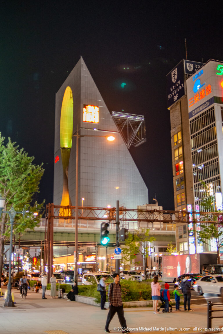 Large Osaka commercial building with a tall glowing façade sculpture at night.