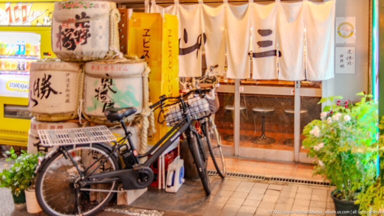 Bicycle parked outside an Osaka restaurant with white noren curtains and sake barrels.