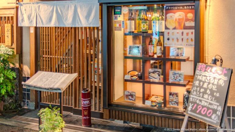 Wooden Osaka restaurant entrance with glass menu display and handwritten chalkboard.