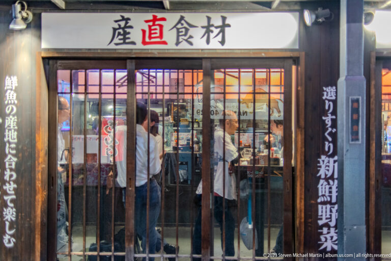 Wood-framed Osaka seafood restaurant entrance with Japanese signs advertising fresh ingredients.
