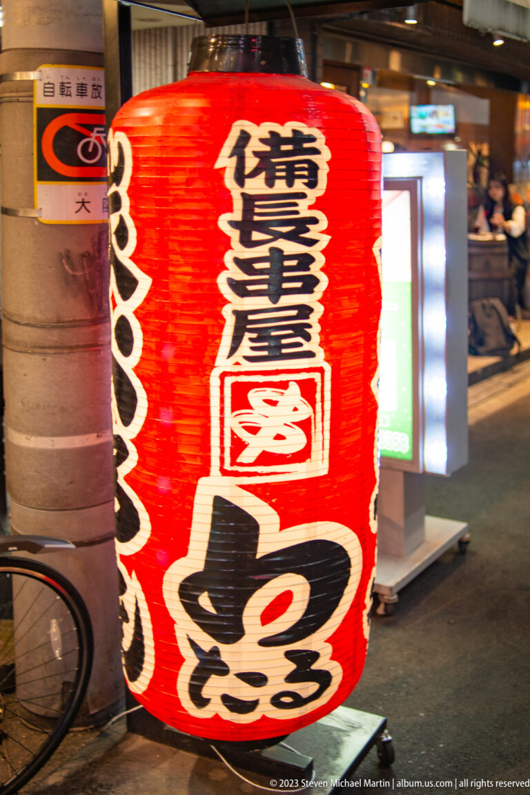 Large red restaurant lantern with black calligraphy and an octopus motif in Osaka.